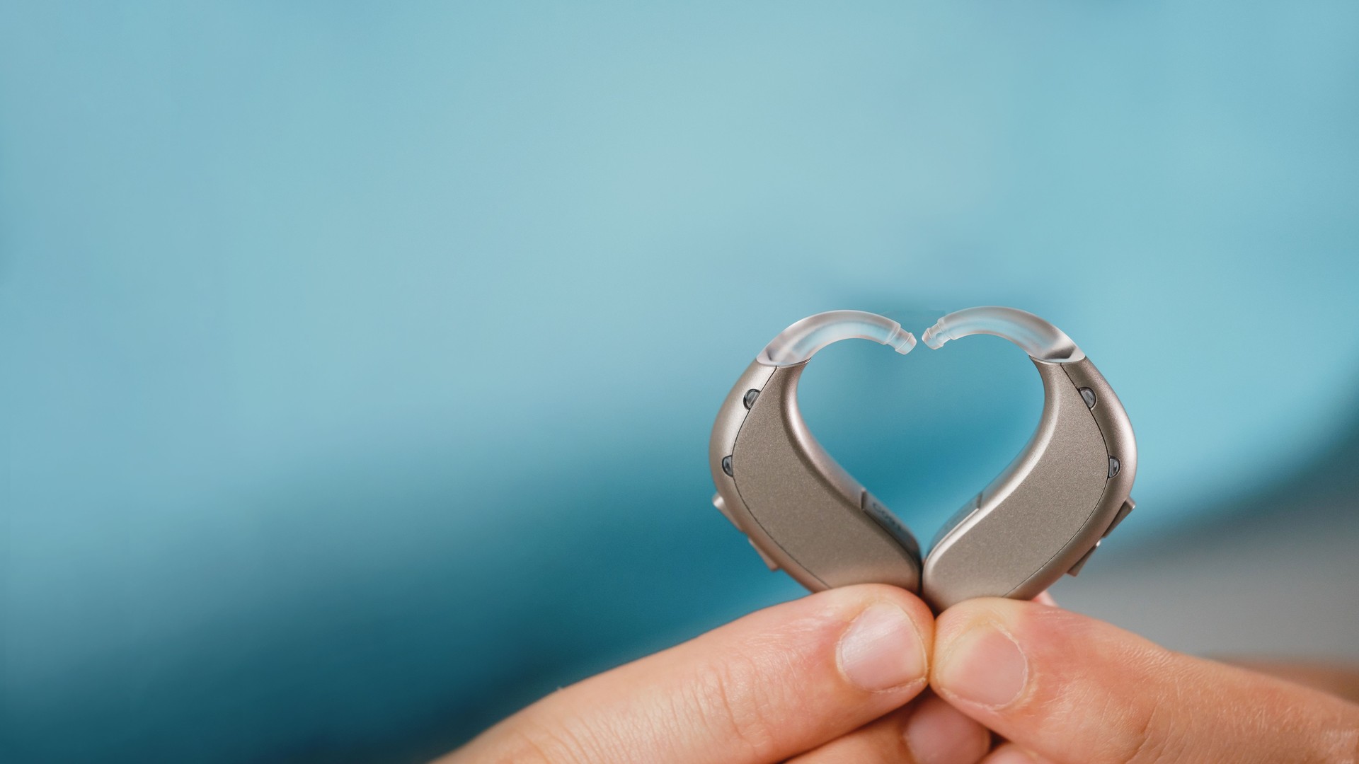 Hearing aids in hands making heart shape over blue background