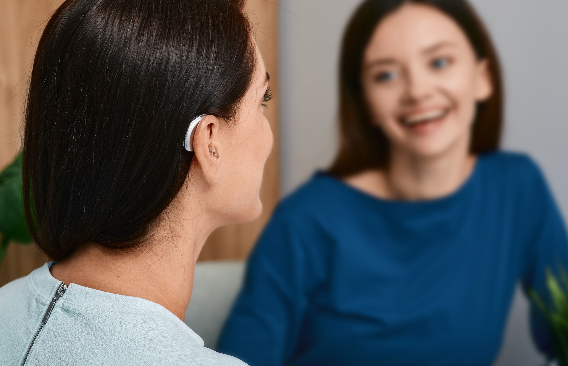 Hearing aids. Woman with hearing aid behind the ear communicates with her female friend at home and leads a fulfilling life with deafness