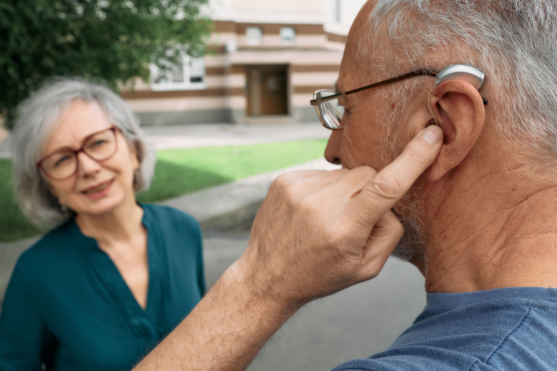 Mature man with a hearing impairment uses a hearing aid to communicate with his female senior friend outdoor. Hearing solutions