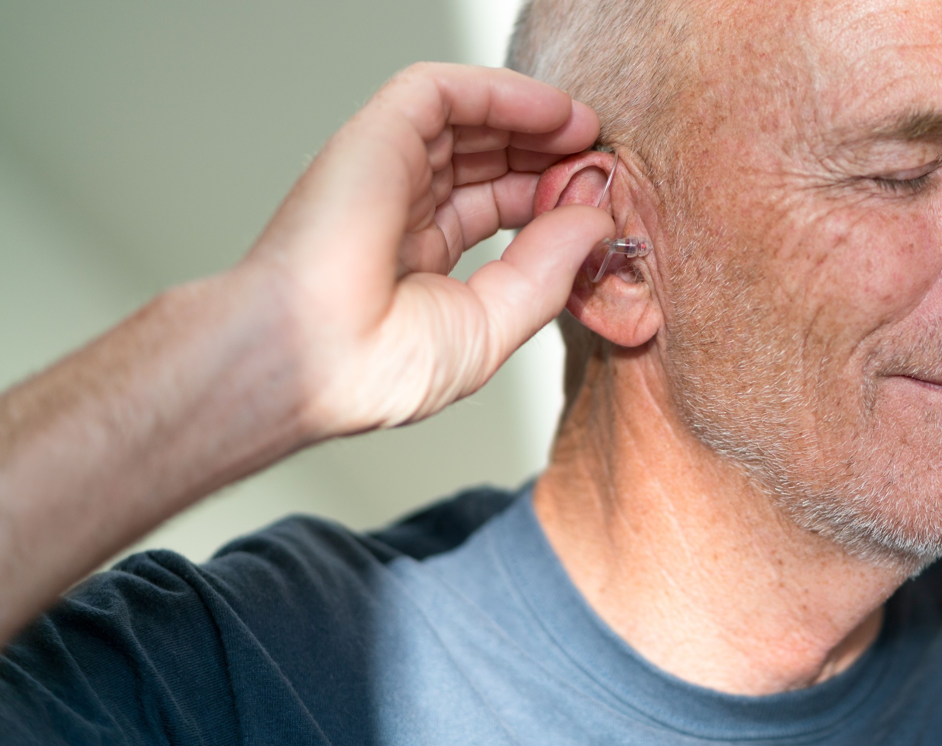 Senior male puts in hearing aid at the start of the day