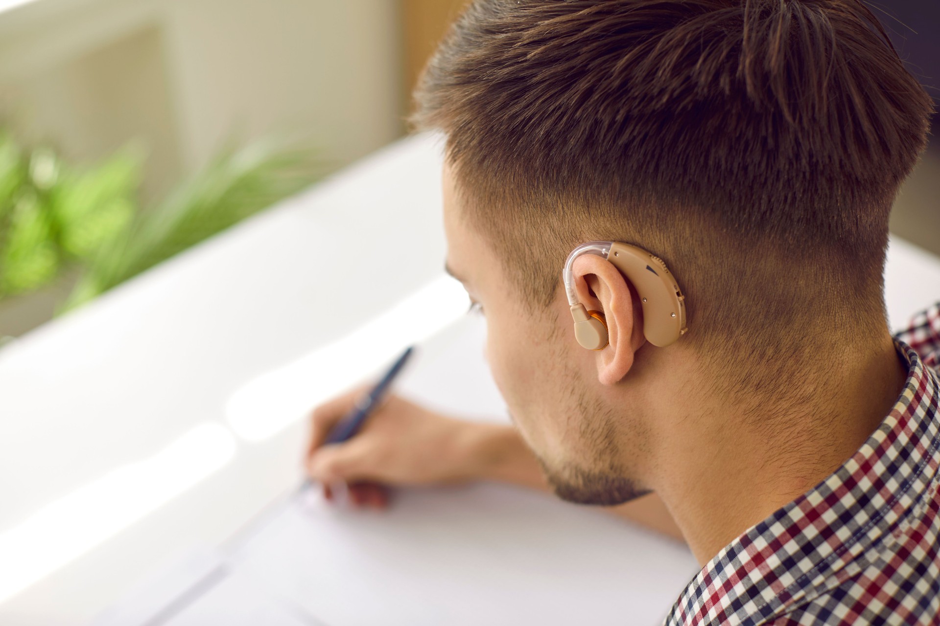 Hearing impaired student wearing modern hearing aid is sitting at desk and writing
